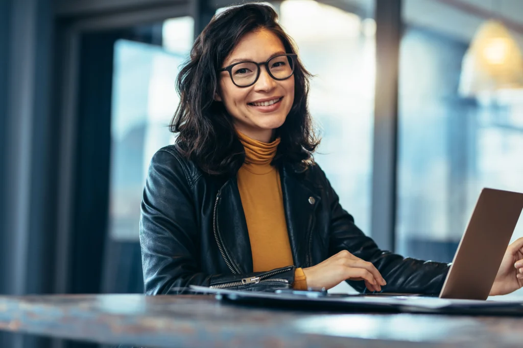 Woman with glasses smiling while working on her laptop